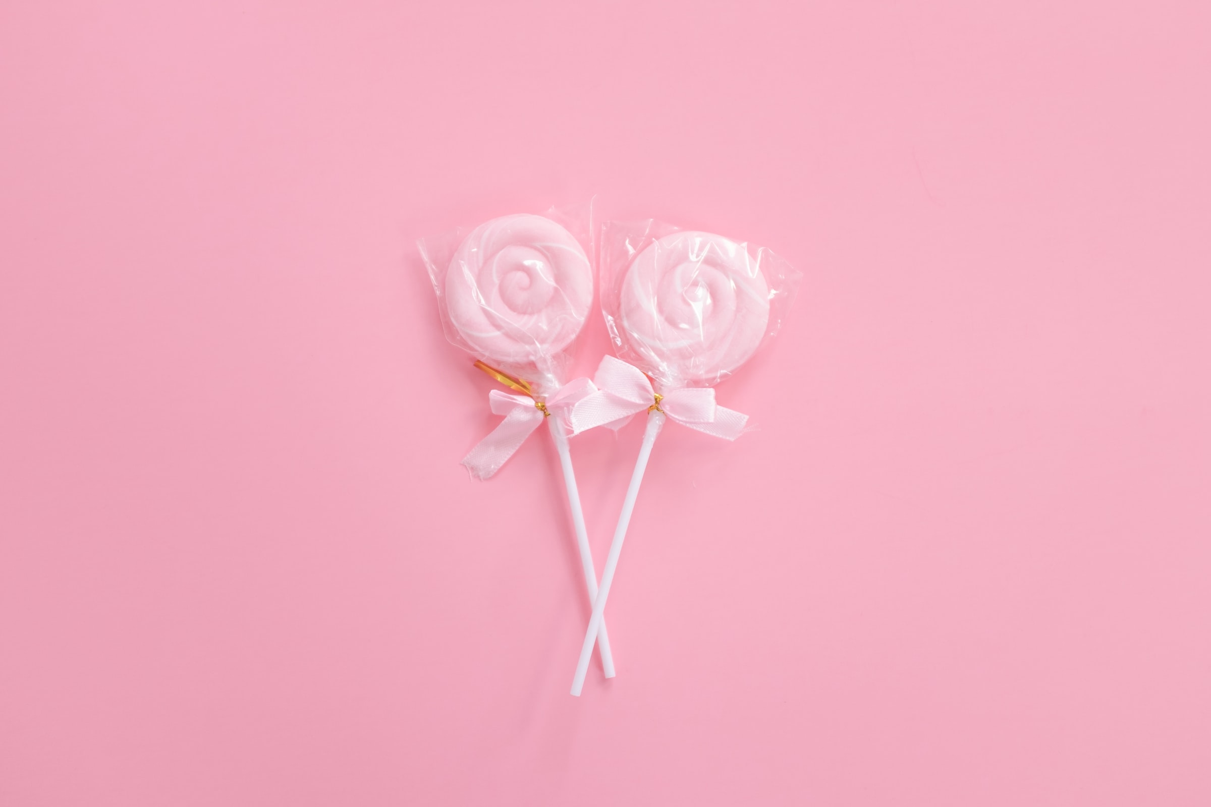Baby pink lollipops wrapped with gold tie and a pink bow against a candy pink background.