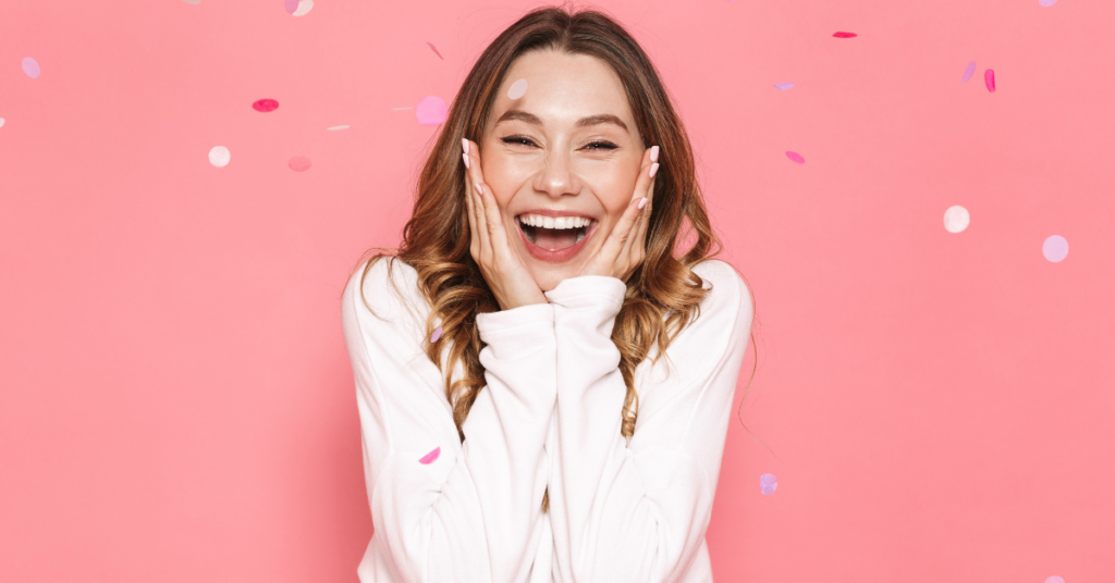 Overjoyed woman holding her cheeks against a pink background with confetti. 
