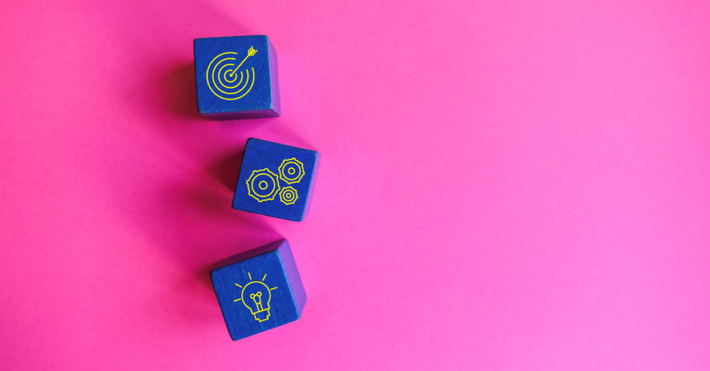Bright pink background with 3 electric blue dice with symbols on them. One is a target and an arrow, the other is a collection of setting icons, and the third is a lightbulb. 