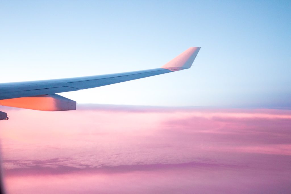 Image of plane flying at sunset over purple and pink clouds