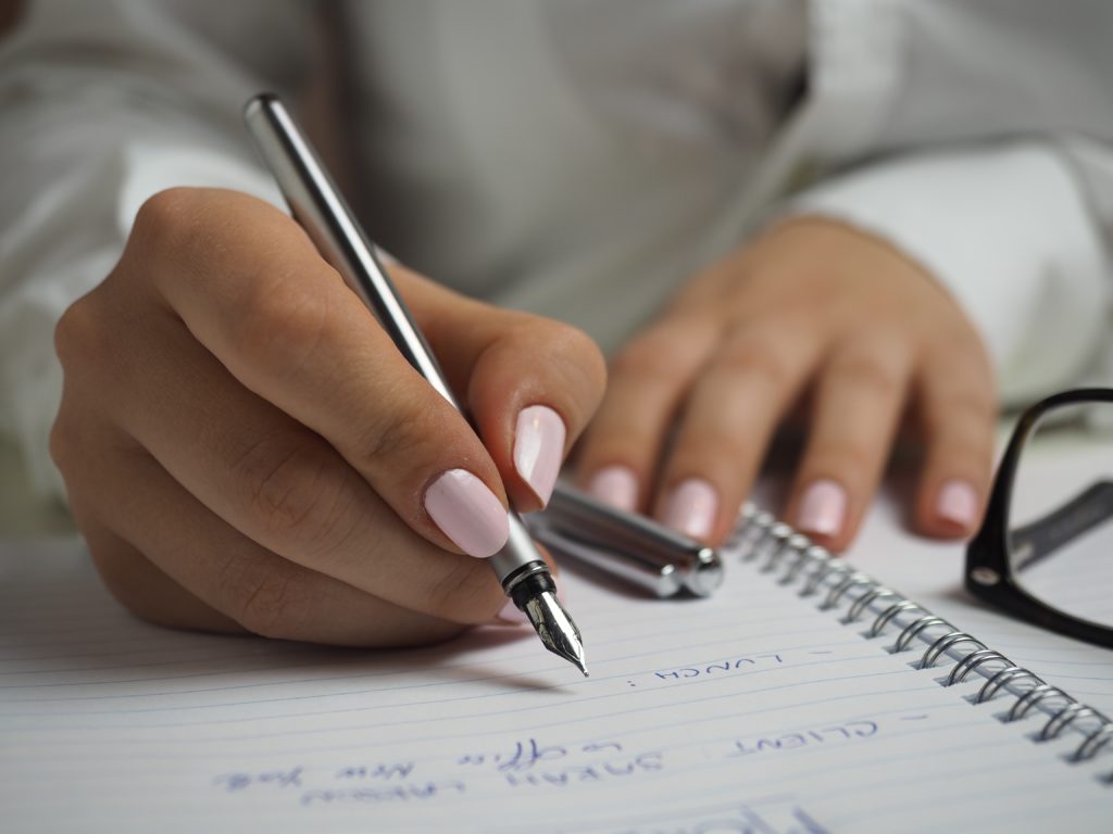 Woman writing in her notebook with a silver fountain pen, with pink polish on nails.