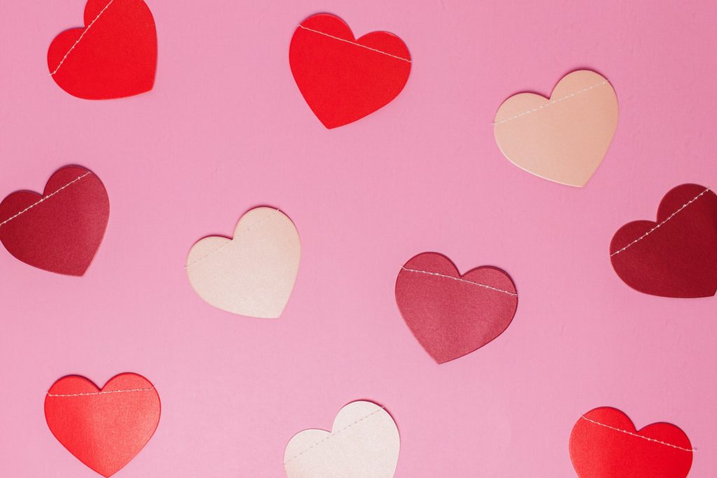 Pink background with 9 silk hearts in shades of red and cream.