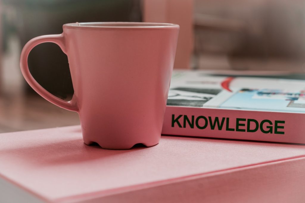 Pink mug and "knowledge" book on another pink book