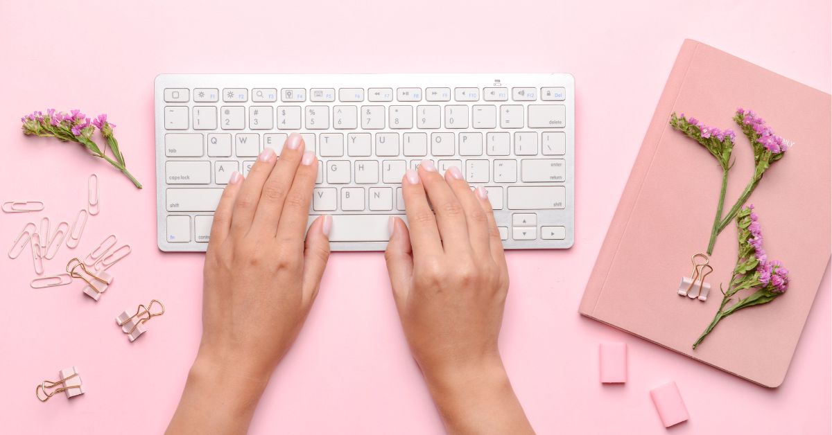 Woman with fingers on PC keyboard, paperclips, a flower, and a notebook.